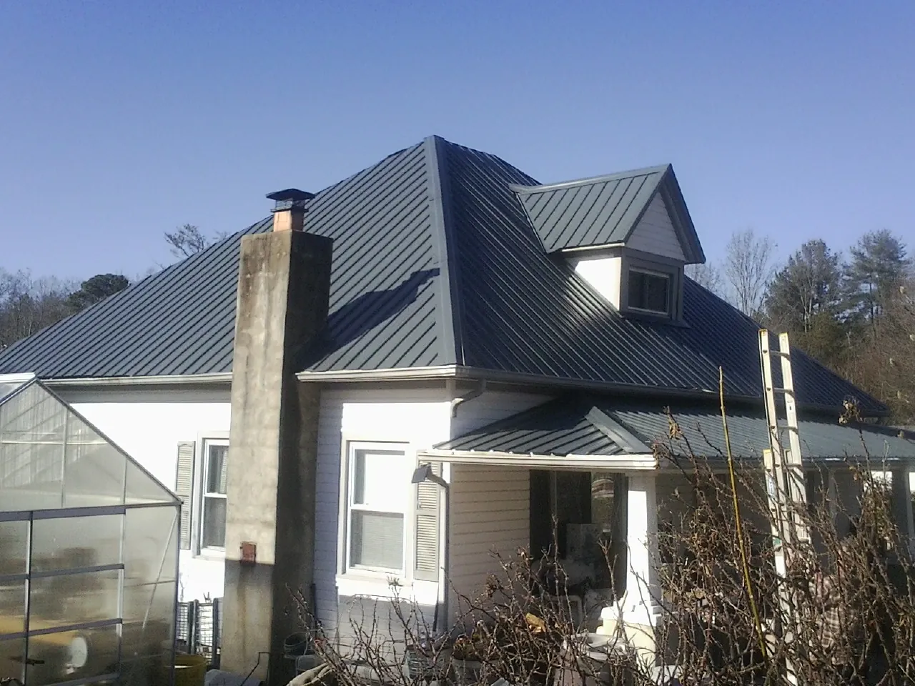 Dark blue standing seam metal roof on a white farmhouse with dormer — Slate & Tile Roof Repair by Roofing Brothers in Henryville