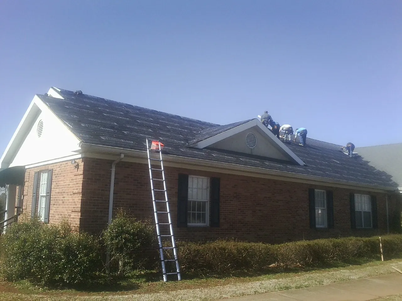 Crew tearing shingles off a brick ranch roof with a ladder set — Metal Roof Repair work by our crew in Henryville