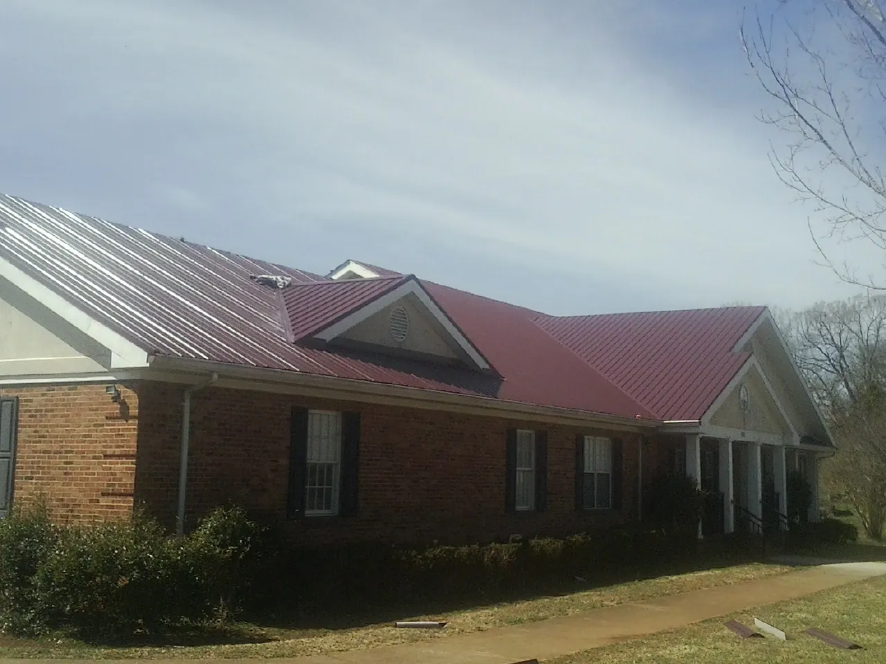 Red metal roof with gabled entries on a long brick building, from a Hail Damage Roof Repair job in Henryville