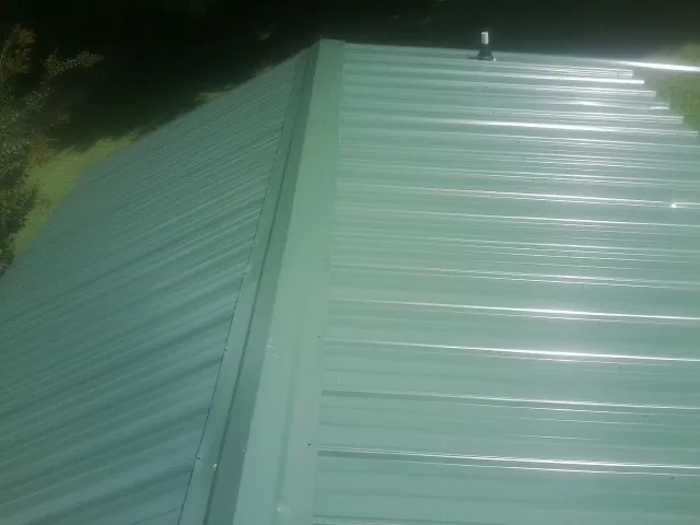 New green metal panels meeting at the ridge of a roof — Flat Roof Repair work by our crew in Henryville