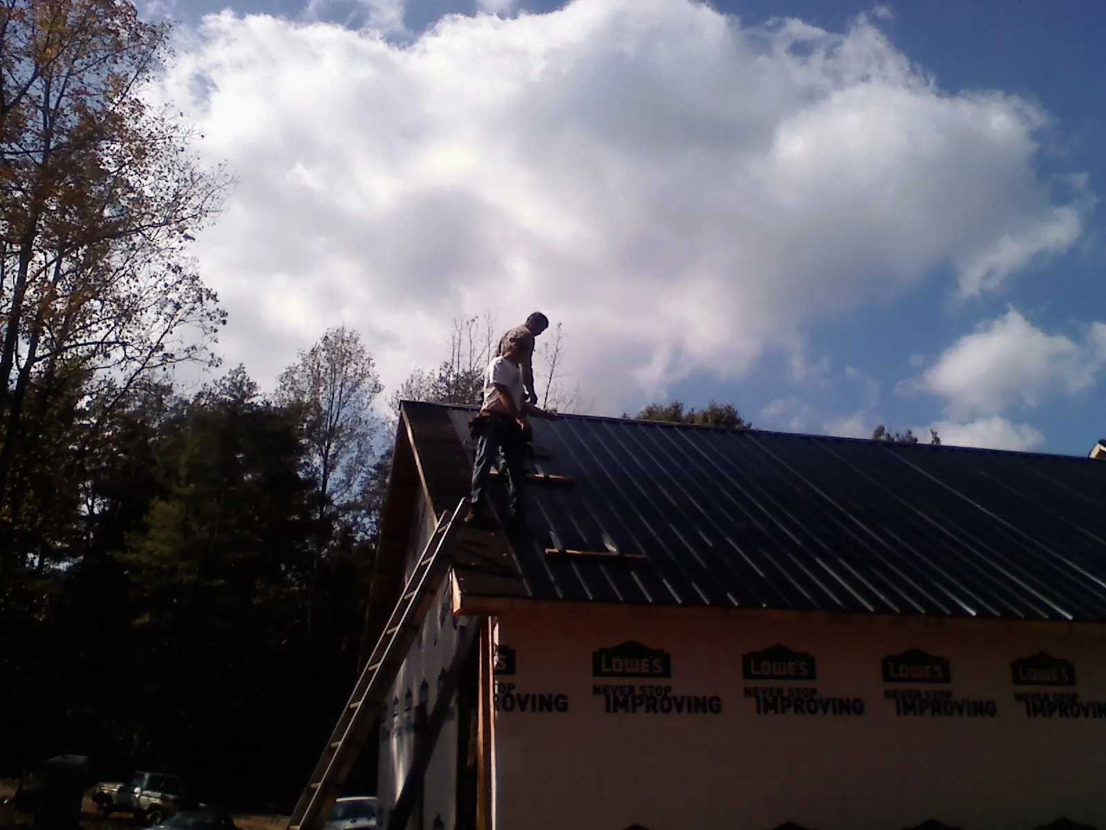 Roofer fastening dark metal panels high against a cloudy sky, from a Roof Inspection job in Henryville