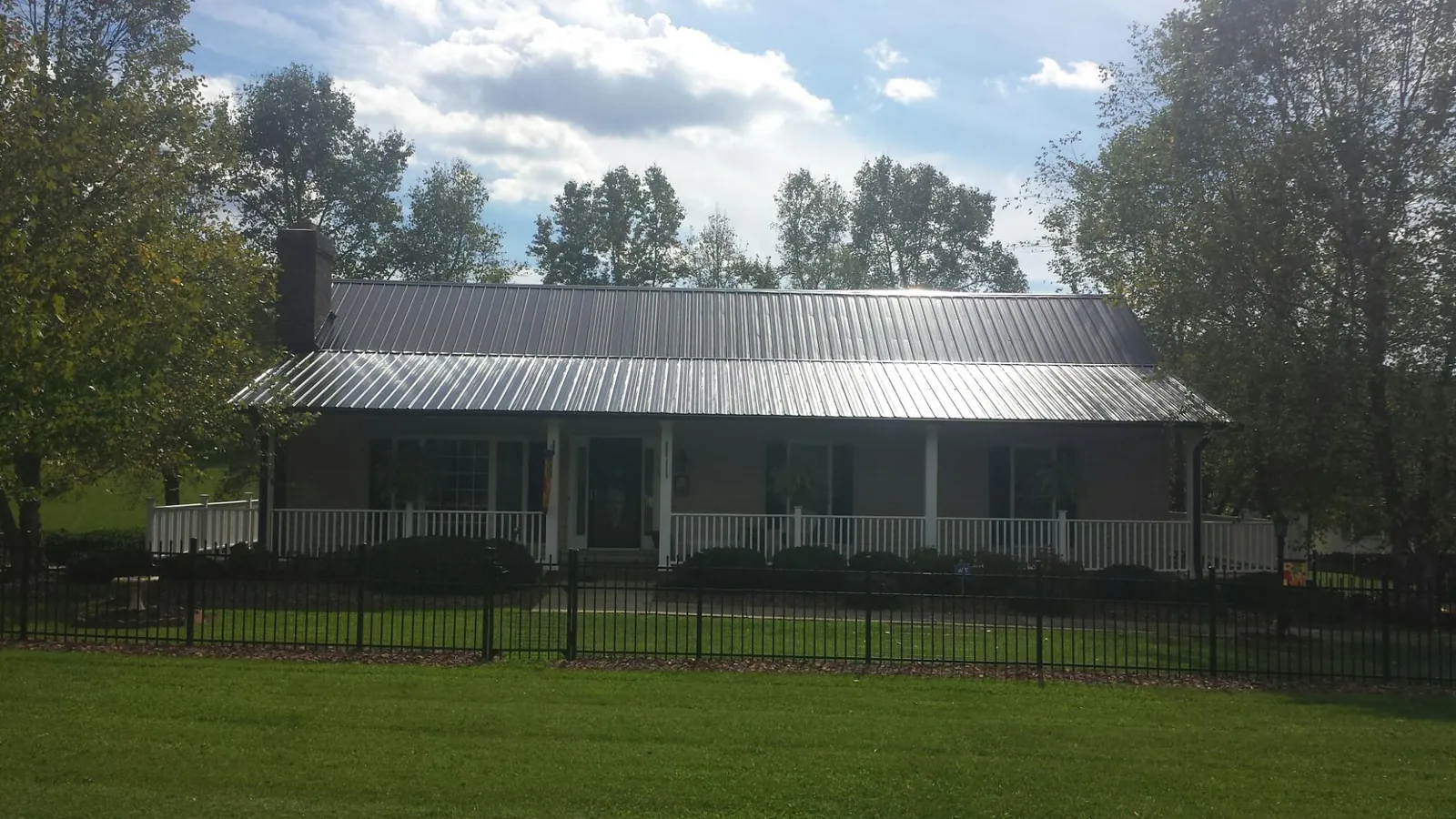 Gray metal roof on a brick ranch with a full width front porch — Gutter Guard Installation work by our crew in Henryville