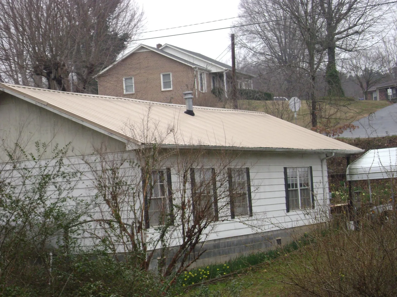 Tan metal roof on a white sided house set into a hillside — Commercial Roofing by Roofing Brothers in Henryville