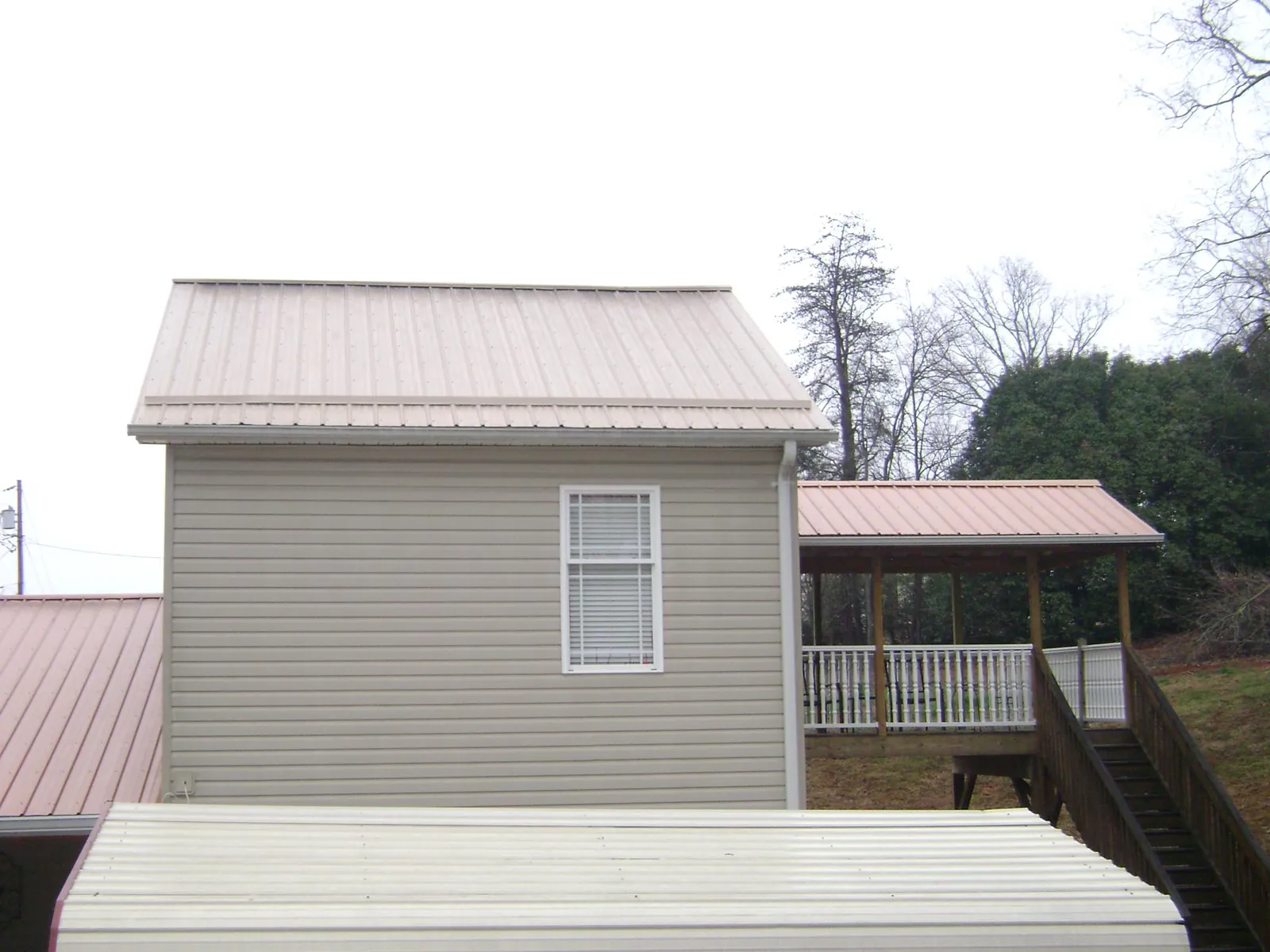Tan metal roofs on a two story addition and attached porch, from a Roof Replacement job in Henryville